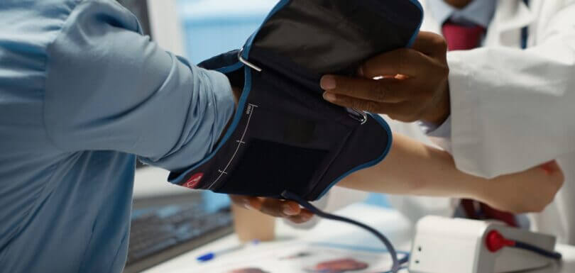 Medical expert taking the pulse and blood pressure with a blood pressure monitor to check hypertension during check up visit, healthcare industry. Physician using modern diagnostic tools for cardiology. Camera a.